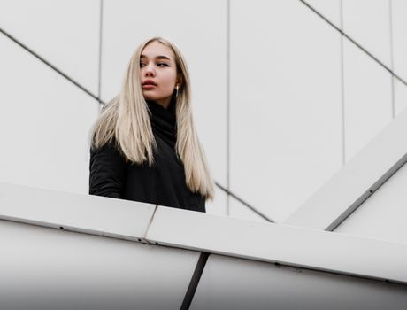 young blonde girl in black clothes against a gray building