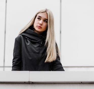 young blonde girl in black clothes against a gray building