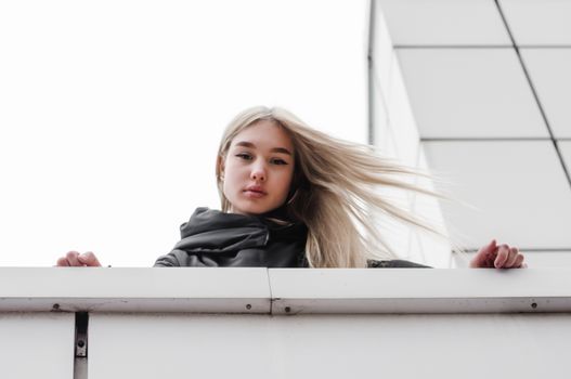 young blonde girl in black clothes against a gray building