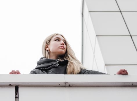 young blonde girl in black clothes against a gray building