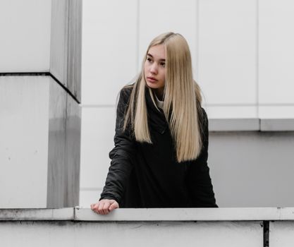 young blonde girl in black clothes against a gray building