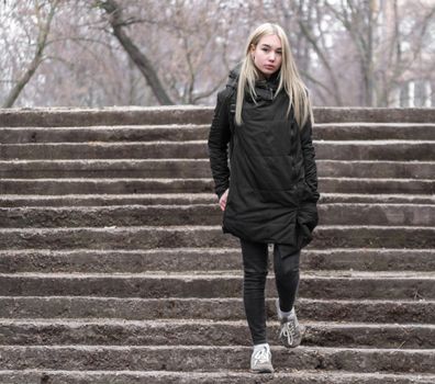 young blonde girl in black clothes comes down the stone stairs