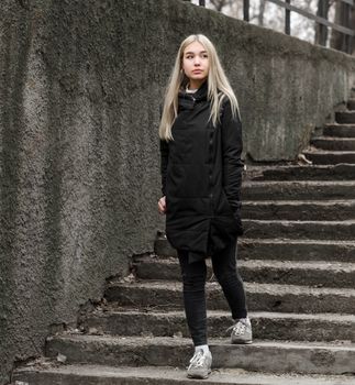 young blonde girl in black clothes comes down the stone stairs