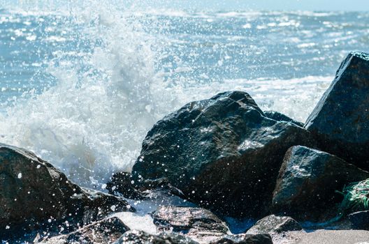 splashes of sea waves on the black stones on the sand of the beach
