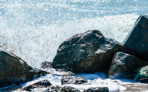 splashes of sea waves on the black stones on the sand of the beach