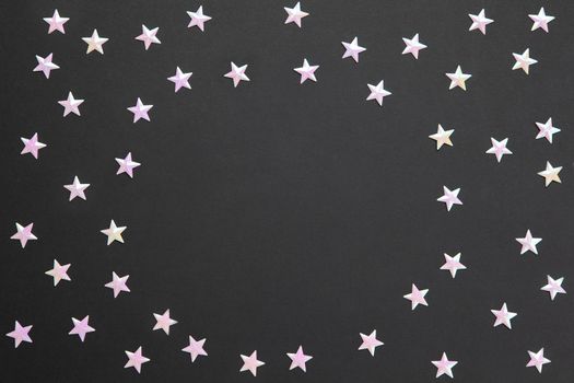 Frame of chaotic numerous pearl confetti in form of small stars on black paper background, copy space. Celebration, holidays, sales, fashion concept. Horizontal. Flatlay. Blank for greeting cards.