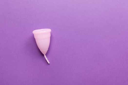 Pink menstrual cup on purple background. Concept zero waste, savings, minimalism, these days. Feminine hygiene product, flat lay, copy space. Horizontal.