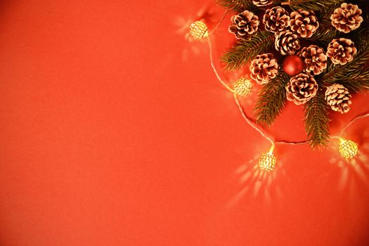 Christmas and New Year composition. Seasonal greeting card concept with pinecones, evergreen branches and lights on red background. Christmas, winter, new year concept. Flat lay, top view, copy space. 