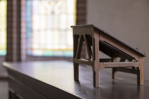 Wooden lectern in an old church with stained glass windows in the background
