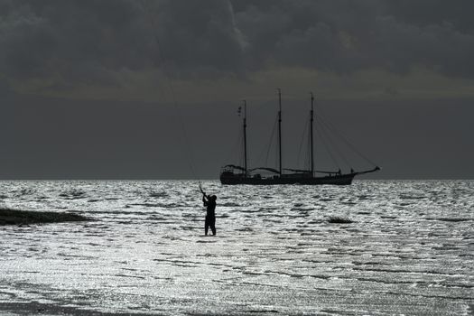 Contour of a three-masted sailboat and a kite surfer on the Wadden Sea near the island of Terschelling in the North of the Netherlands
