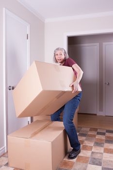 Grey haired woman in her early fifties lifting a huge cardboard box while she's moving to other house