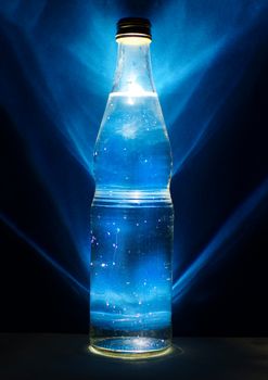 Glass bottle with mineral water. Bottle on blue background with backlight.