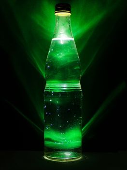 Drink in a glass bottle with green background and backlight. Alcoholic beverage. Harm to health. Healthy lifestyle. A bottle of alcohol and the drops of condensate. Cold drink.