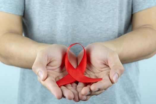 Aids awareness, male hands holding red AIDS awareness ribbon. World Aids Day, Healthcare and medical concept.