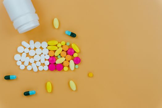 Assorted pharmaceutical medicine pills, tablets and capsules, and bottle on yellow background. Copy space for text, top view.