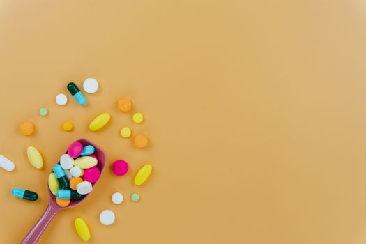 Assorted pharmaceutical medicine pills, tablets and capsules, and spoon on yellow background. Copy space for text, top view.