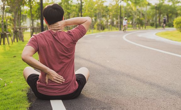 A male athlete suffering from neck and back pain and injury at the park. Sport and healthcare concept.