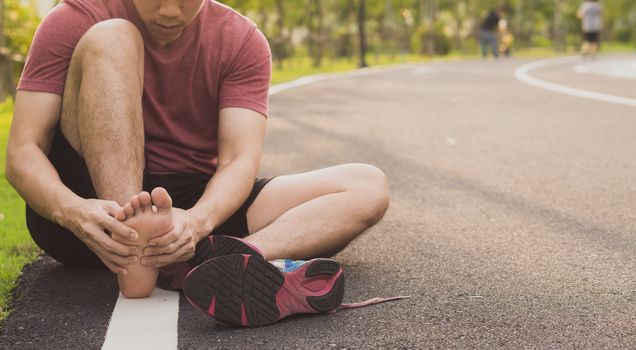 Young man massaging his painful foot from jogging and running on running track. Sport and exercise concept.