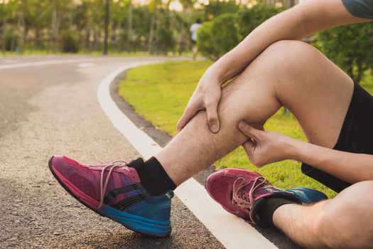 Young man massaging his painful leg from jogging and running on running track. Sport and exercise concept.