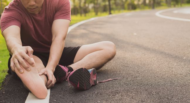 Young man massaging his painful foot from jogging and running on running track. Sport and exercise concept.