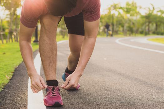 The male athlete is tying running shoes in the park with sunlight. Sport and exercise concept.