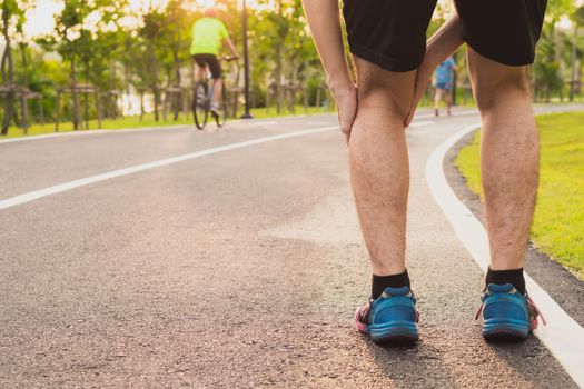 Knee Injuries. Young sport man holding knee with his hands in pain after suffering muscle injury during a running workout at park. Healthcare and sport concept.