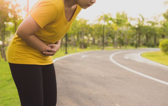 Sport womanman holding abdomen with her hands in stomach pain after running workout at park. Health care concept