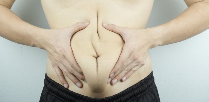 Close up man holding excessive fat belly on white background. Diet, weight loss, slim body, healthy lifestyle concept.