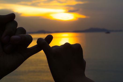Silhouette of hand to pinky promise, pinky swear in front of the sun during sunset time. Love and valentine concept.