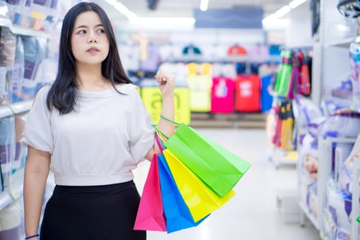 Pretty smiling Asian woman holding many shopping bags in the shopping mall. Shopping concept.