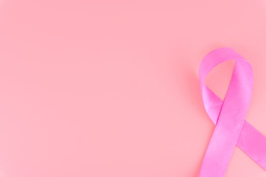 Pink ribbon breast cancer on pink background with copy space for text. Flat lay, top view.