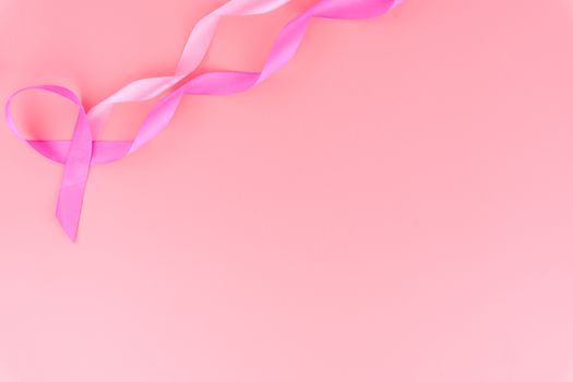 Pink ribbon breast cancer on pink background with copy space for text. Flat lay, top view.