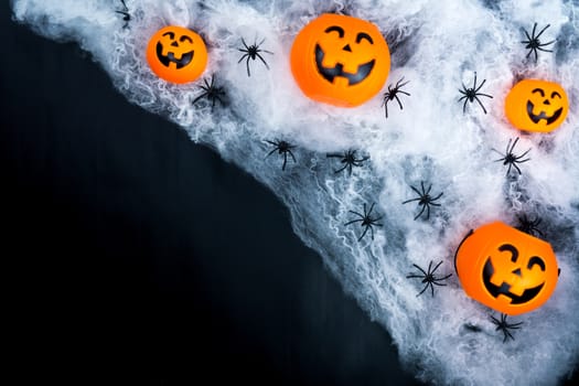 Halloween holiday background with spider, webs and jack lantern on black background with copy space for text. Flat lay, top view