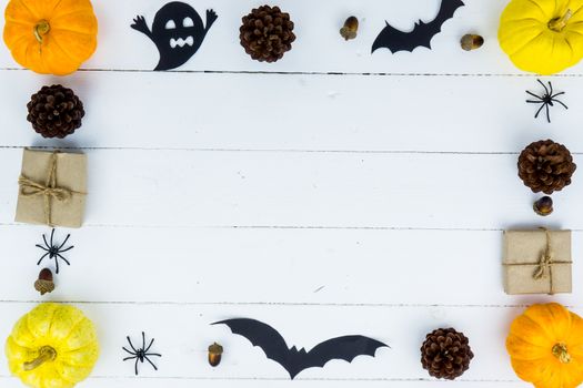 Halloween holiday background with orange pumpkin, ghost, spider and bat on white wooden table with copy space for text. Flat lay, top view