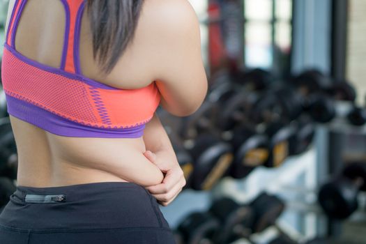 Close up woman holding excessive fat belly at fitness gym. Diet, weight loss, slim body, healthy lifestyle concept.