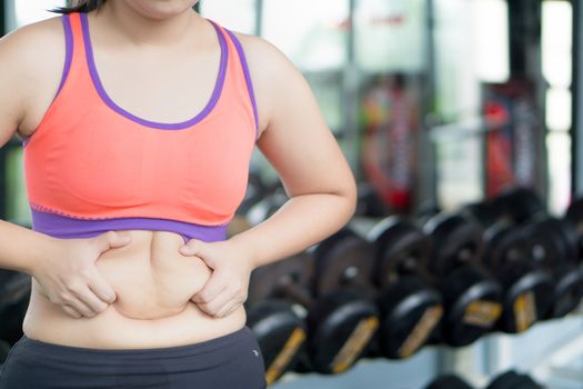 Close up woman holding excessive fat belly at fitness gym. Diet, weight loss, slim body, healthy lifestyle concept.