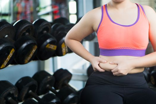 Close up woman holding excessive fat belly at fitness gym. Diet, weight loss, slim body, healthy lifestyle concept.