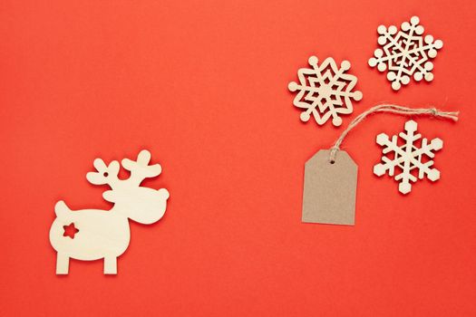 Christmas decoration, three little wooden snowflakes, craft tag, deer on bright red background. Festive, New Year, sales, eco friendly concept. Horizontal, flat lay. Minimal style. Top view.