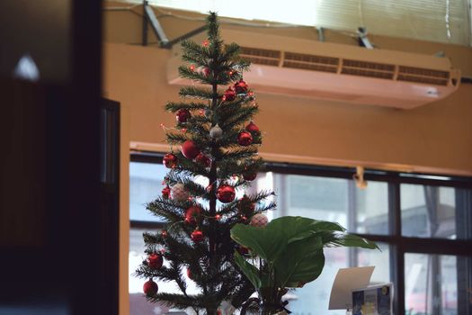 The Festive green Christmas tree decorated with gold and red toys balls and bows with soft focus in evening and beautiful dark blurred defocused sparkling background with golden highlights, copy space.