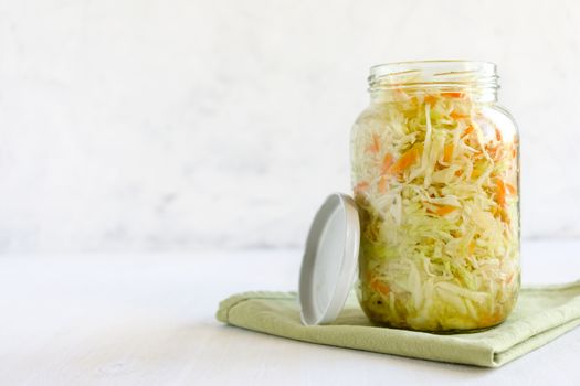 Sealed glass jar with delectable fermented cabbage standing on piece of cloth on white background