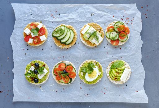 Assorted tasty appetizers with fresh vegetables, feta cheese and egg on crumpled paper viewed from overhead in two neat rows