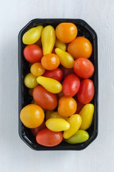 Black tray of fresh homegrown tomatoes of different colors, viewed from above on white wooden background