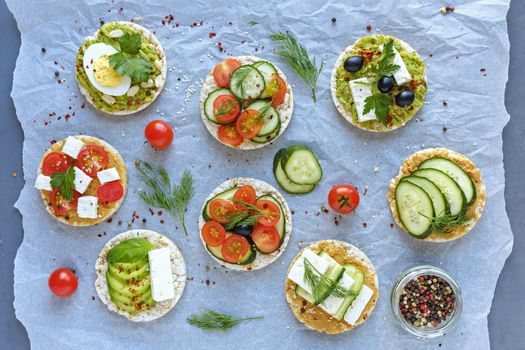 Gourmet selection of fresh appetizers or snacks arranged on crumpled paper in an overhead view with fresh vegetables, cheese and herbs on crackers