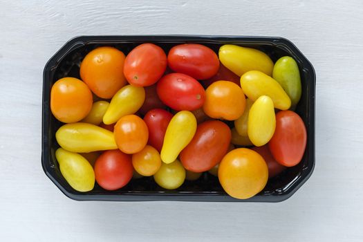 Black tray of fresh homegrown tomatoes of different colors, viewed from above on white wooden background