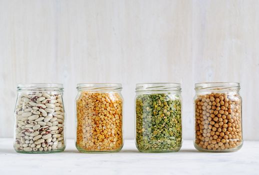 Died haricot beans, lentils and chickpeas in glass kitchen jars in a row against a white wall with copy space