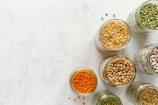 Colorful healthy dried legumes in glass jars over a textured white background with copy space viewed from overhead