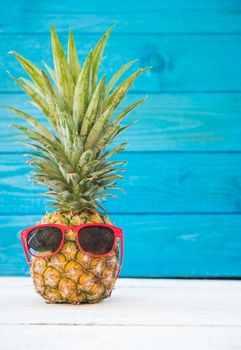 Holiday pineapple have sunglasses on blue wooden background, tropical holiday concept
