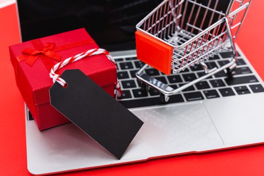 Internet online shopping marketing, top view of workspace with blank black tag, gift box and cart shopping on laptop computer on red background and have copy space for use