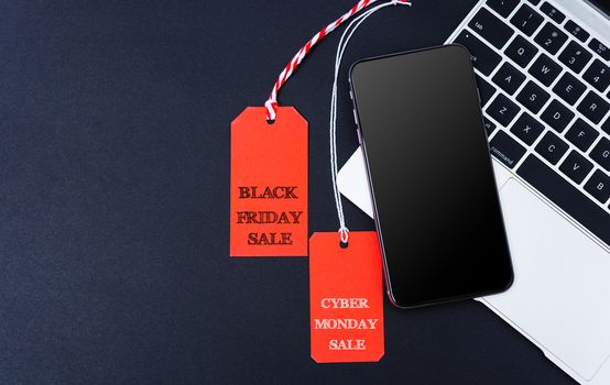 Online shopping Cyber Monday sale text and Black Friday Sale text on both red tag near smart phone and laptop computer with black background