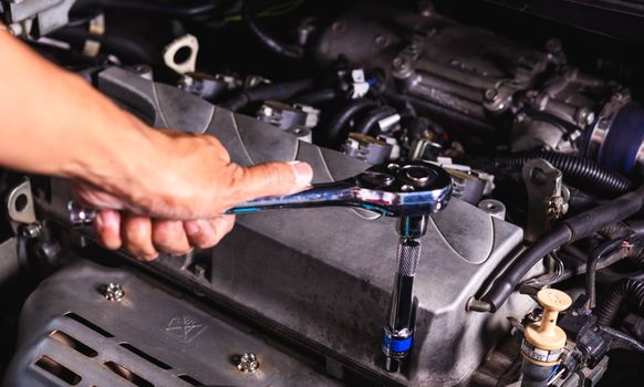 Hand of auto mechanic technician service engine and using wrench socket repairing car in garage